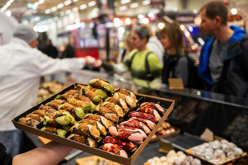 Auf einer Messe hält eine nicht gezeigte Person einen Teller mit Cannoli hoch